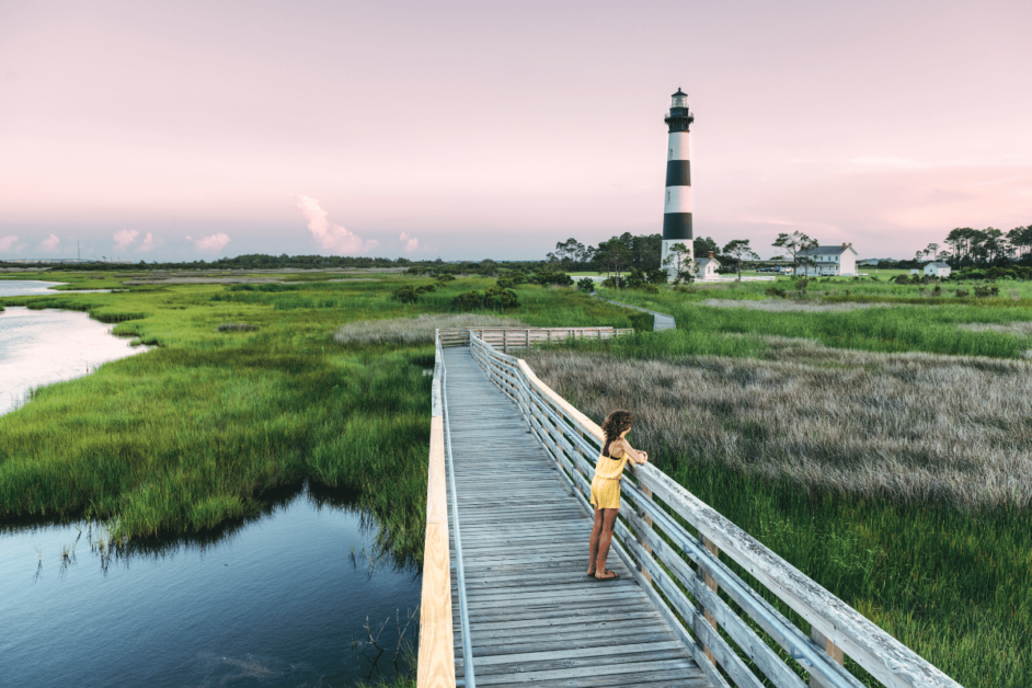 girl standing on pier in the outer banks with lighthouse in the background