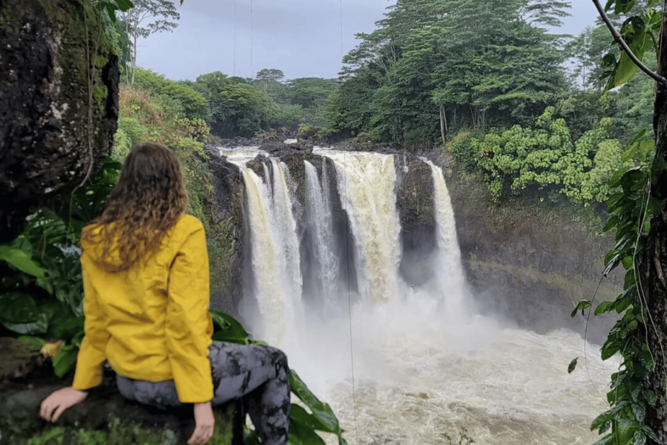 Girl wearing yellow rain jacket on day hike in Hawaii with a waterfall in the background.