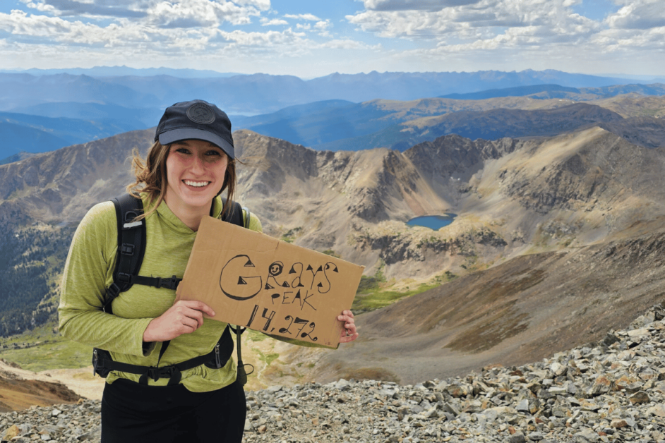 girl holding sign at the tops of grays peak in colorado 