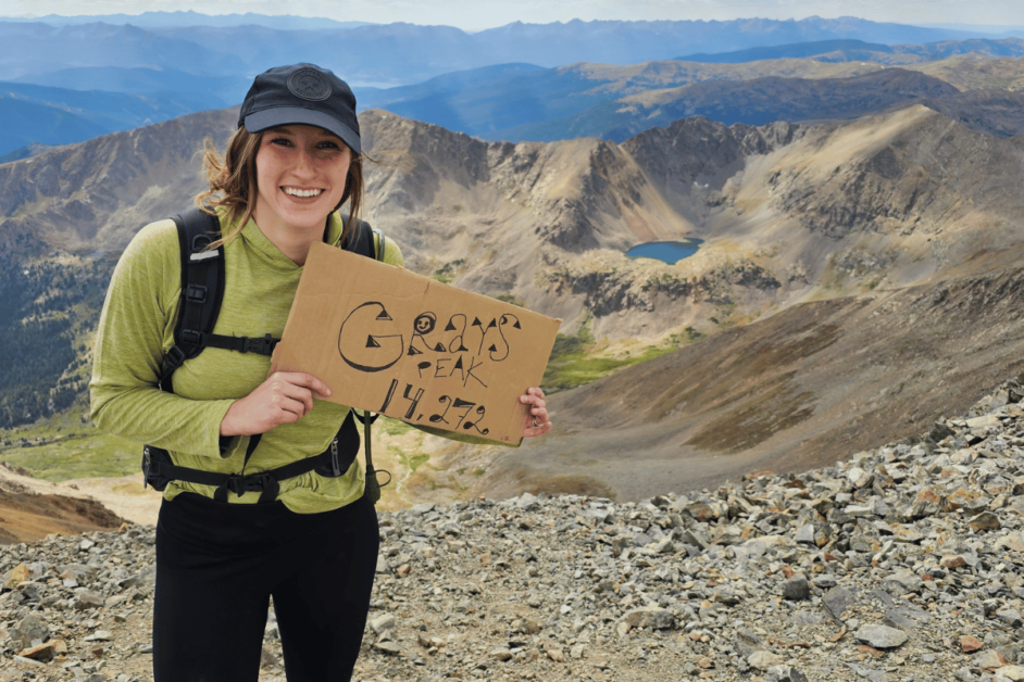 girl holding a sign at the top of Gray's Peak 