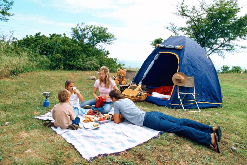 fun things for families to do while camping- mom, dad, and two kids having a picnic in front of their tent. 