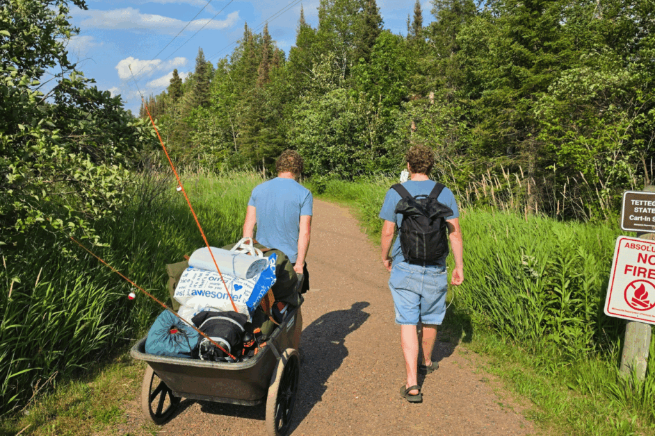 2 people carrying a cart with camping gear.